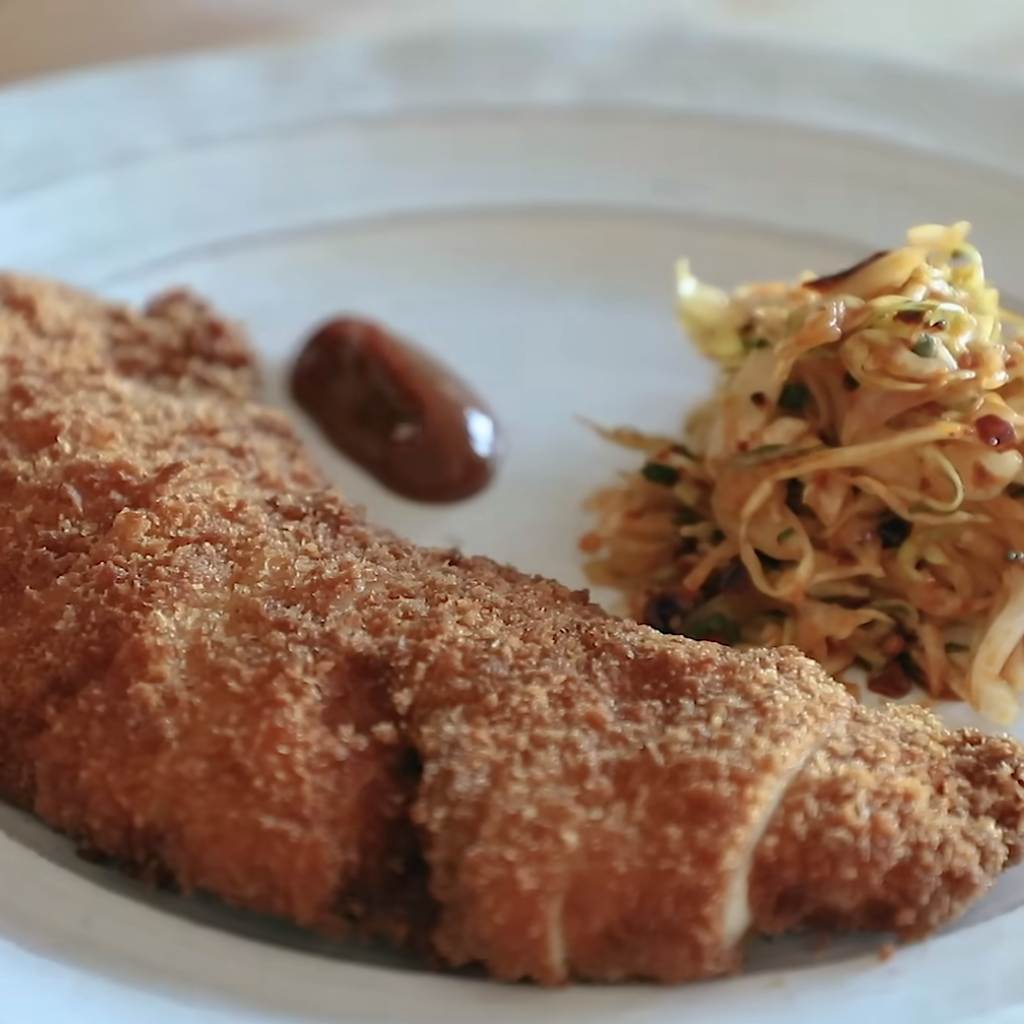 This image shows chicken katsu ready to serve in a dish with sauce and cabbage