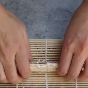 this image shows rollig all the ingredients into a tight sushi roll Using a bamboo mat