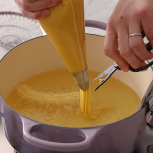 This image shows dough to a pastry bag with a star tip and pipe 5- to 6-inch strips into hot oil in batches for churros