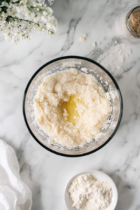 Cooked and mashed lentils being blended with olive oil and water in a blender on a marble countertop, resulting in a smooth, creamy mixture.