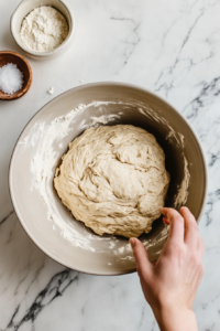 A large mixing bowl where the lentil mixture, flour mixture, and yeast mixture are being combined, with a hand kneading the dough until smooth and elastic