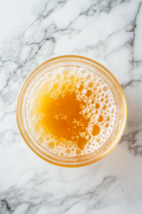 A small bowl with yeast dissolving in warm water and honey on a marble countertop, beginning to foam as it activates.