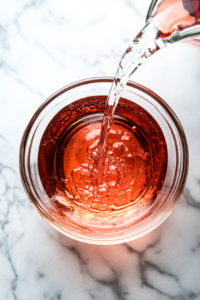 Clear cherry-infused liquid being poured into a 1-quart jar on a marble countertop, ready for storage with the sediment left behind.