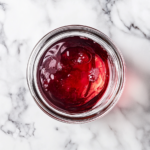 Clear cherry-infused liquid being poured into a 1-quart jar on a marble countertop, ready for storage with the sediment left behind.