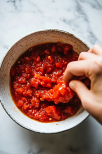 the image shows Crushing Canned Tomatoes for Marinara Sauce