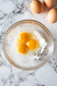 Whisking egg yolks and sugar together in a mixing bowl until they form a pale, creamy mixture, ready to be incorporated into the Natilla custard.