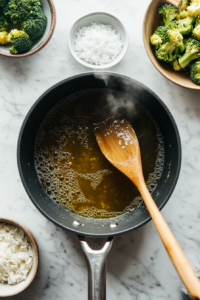 Broth boiling in a medium saucepan with white rice and chopped broccoli florets being added, part of the Creamy Broccoli Cheddar Rice Recipe.