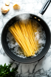 A pot of salted water on the stovetop with linguine being submerged, preparing the pasta for the linguine bolognese dish.