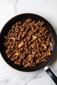 Ground beef browning in a skillet with seasonings, creating a rich base for the linguine bolognese sauce.