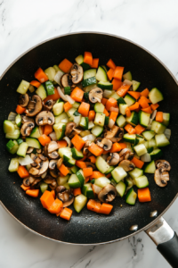 Sautéed diced vegetables, including onions, zucchini, carrots, and bell peppers, browning in a large skillet for the linguine bolognese sauce.