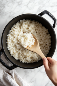 Steaming hot rice being fluffed with a wooden spoon after cooking to ensure light, airy texture for Chimichurri rice.