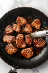 Thin slices of marinated beef sizzling in a hot skillet, frying to a crisp golden-brown in oil, with bubbles rising around the edges of the meat.