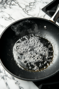 A large non-stick skillet with oil being heated over medium-high heat, prepared for frying the flour and egg-coated meat jun slices to golden perfection.