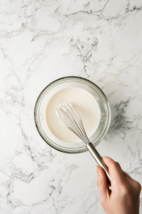 Cornstarch being mixed smoothly into warm milk to create a slurry, ensuring no lumps form for the Cuban Natilla recipe.