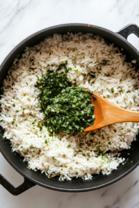 Chimichurri sauce being gently mixed into fluffy white rice with a wooden spoon, combining the fresh herbs and tangy flavor into the rice.