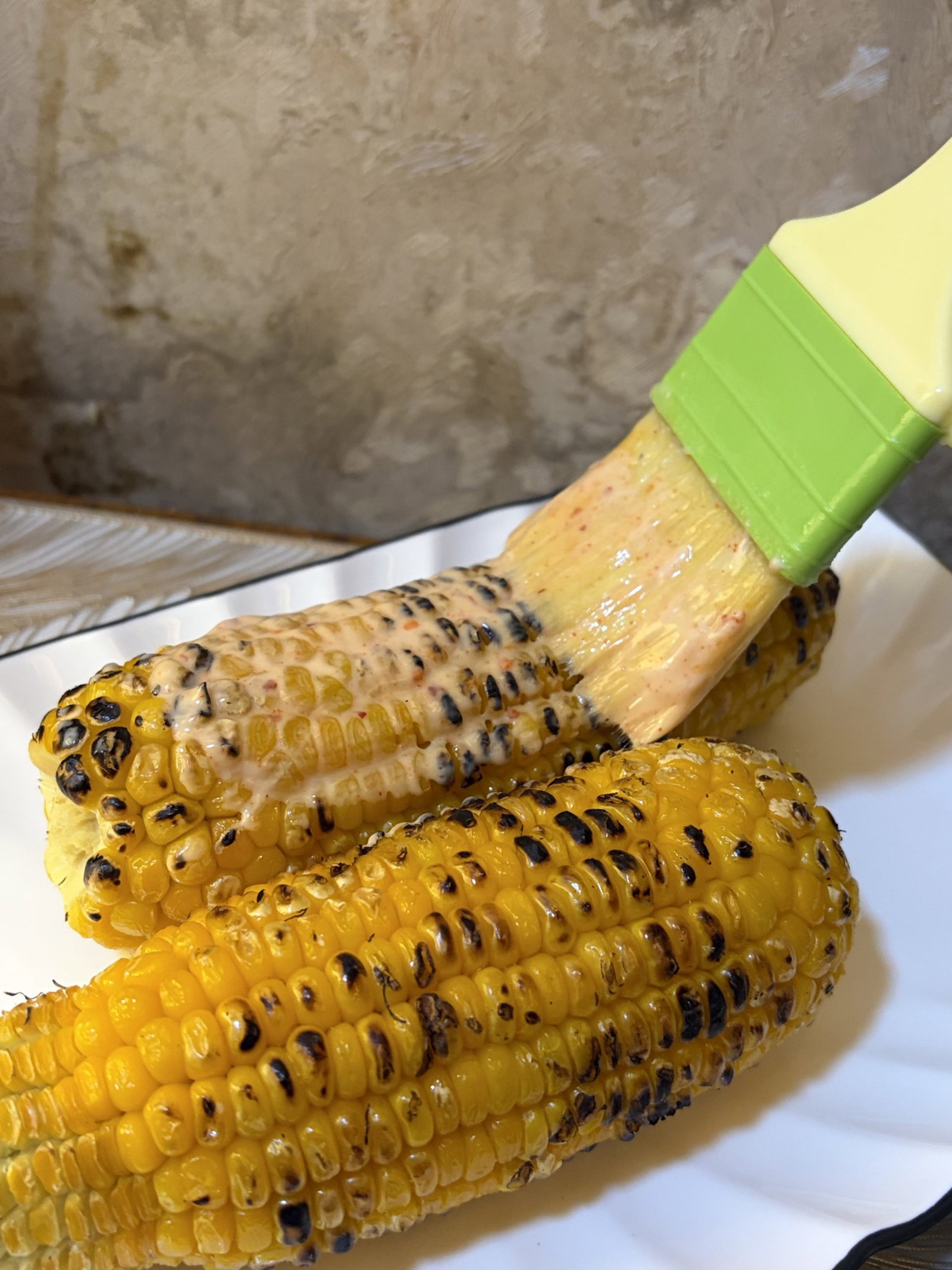 Once the corn is charred and cooked through, use a brush or spoon to generously coat one cob with the mayo mixture.
