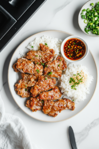 A beautifully plated serving of meat jun with hot white rice, garnished with green onions and served alongside a tangy dipping sauce, offering a complete Hawaii-style meal experience.