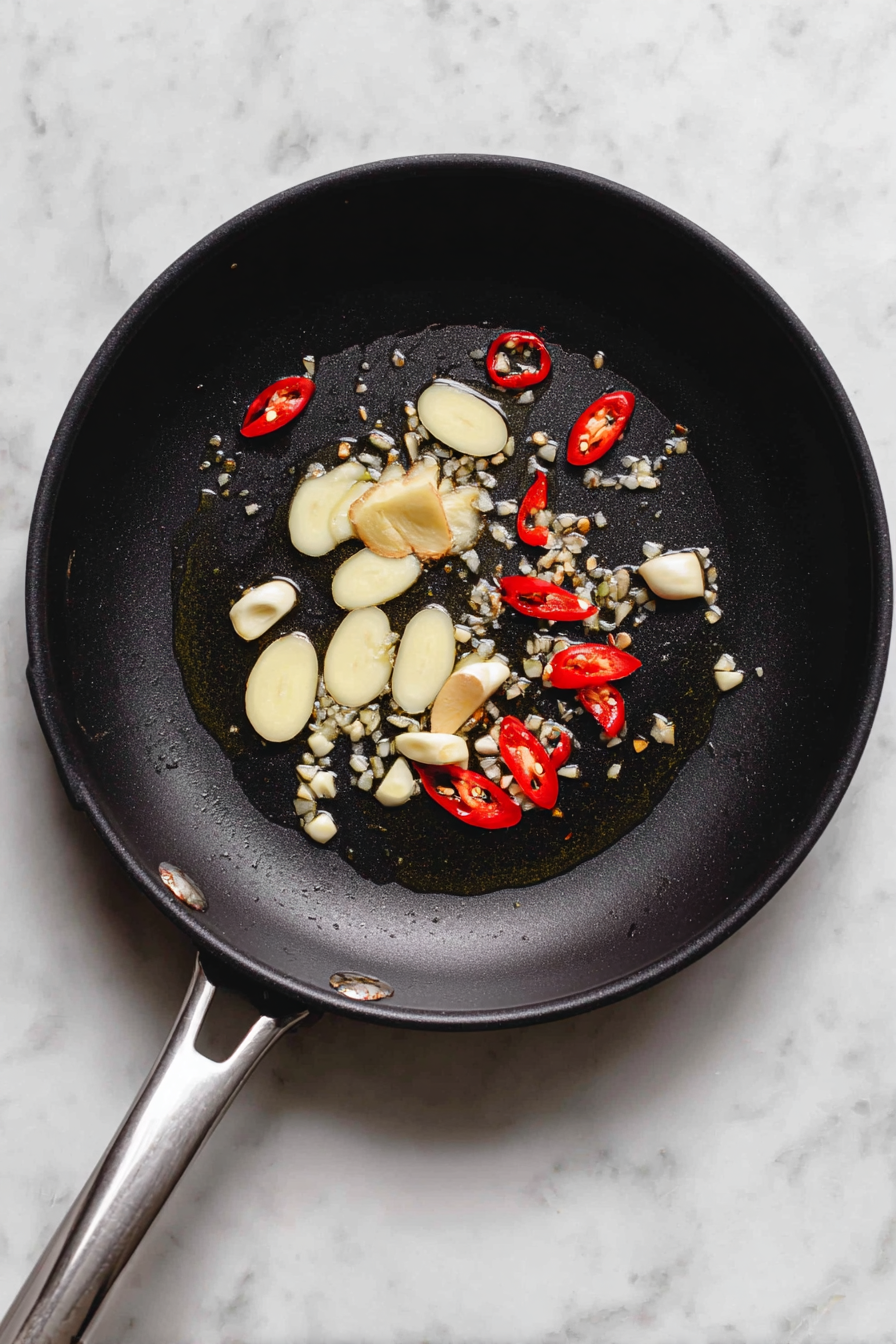 Heat oil in a wok or skillet over medium heat. Add garlic, ginger, and red chilies. Stir-fry until fragrant.