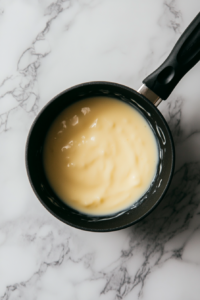 Stirring the custard mixture in a saucepan as it thickens to a smooth, creamy texture, forming the base of the Cuban Natilla dessert.