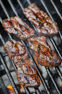 This image shows marinated flap steak being seared on a high heat charcoal grill, achieving a perfect char and sear on the meat.