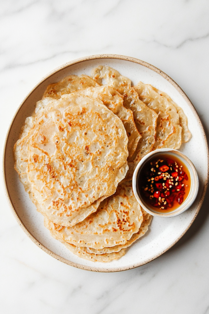  This image shows crispy rice pancakes served with a side of fresh fruit and a small dish of honey, all displayed on a white plate with a clean marble cooktop setting.