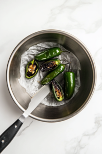 This image shows the blackened skins of charred jalapeños being peeled off, with the seeds and membranes being removed, preparing them for the marinade.