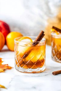 Garnishing Autumn Rum Old Fashioned with cinnamon stick and orange peel twist