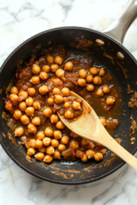 The chickpea stir-fry sauce gently simmering in a skillet, slowly thickening to the perfect consistency while the chickpeas cook.