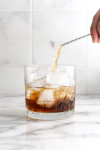 Straining the chilled Autumn Rum Old Fashioned into a rocks glass with ice