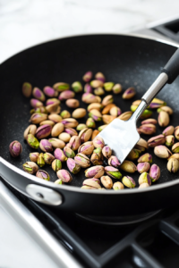 Pistachios toasting in a skillet and being chopped for salad topping.