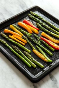 Fresh asparagus spears and baby bell peppers tossed in olive oil, placed on a sheet pan, ready for roasting in the oven for 15-20 minutes