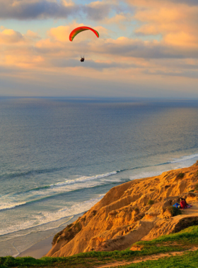 A breathtaking view of Torrey Pines Gliderport in La Jolla, San Diego, overlooking cliffs and the Pacific Ocean. The image shows paragliders taking off into the open skies, with scenic coastal cliffs in the background. Known for its panoramic views, Torrey Pines Gliderport is a prime location for adventure sports and sightseeing.