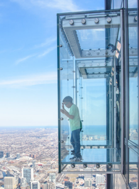 A breathtaking view from Skydeck Chicago, located on the 103rd floor of the Willis Tower. The image captures the expansive skyline of Chicago, with a panoramic perspective over the city and beyond. Visitors can experience the thrill of standing on the glass ledge, creating an exhilarating sense of openness above the bustling streets.