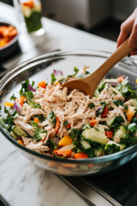 This image shows shredded cooled chicken being prepared. The chicken is shredded into large pieces for the chicken salad.