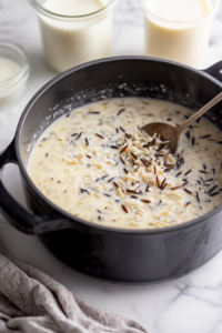 Cooked wild rice spooned into black pot on marble cooktop, with milk and half-and-half in glass measuring cups nearby, prepared to add creaminess to the soup