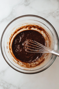 Wet ingredients for pumpkin spice waffles being whisked in a bowl, including eggs, milk, melted butter, pumpkin puree, and vanilla, creating a smooth and creamy base.