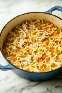 Shredded chicken, half-and-half, and wide egg noodles being stirred into the soup, thickening to a creamy chicken noodle consistency