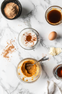 Bowl containing milk, pumpkin purée, egg, maple syrup, vanilla extract, and melted butter being whisked until smooth to create pumpkin spice pancake batter.