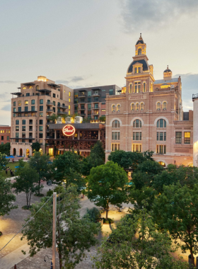 A spacious shopping area with modern architectural elements and landscaping, offering a mix of open-air walkways and shops, inviting people to enjoy a leisurely shopping experience.

