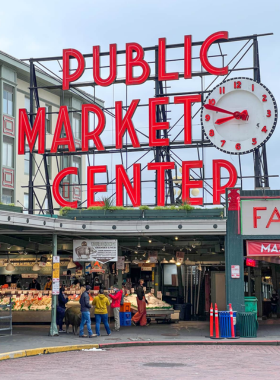 The iconic neon sign of Pike Place Market, with people milling about in the background. The historic market, known for its fresh produce and artisanal goods, is a cultural staple of Seattle.