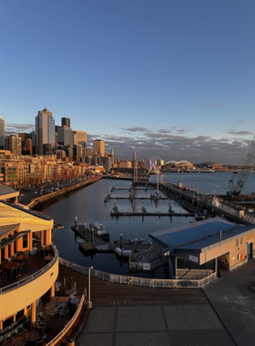 A bustling area along the Seattle waterfront, featuring restaurants, shops, and people enjoying the scenic surroundings. The vibrant setting combines urban life with waterfront beauty.