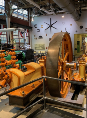 A large, black steam engine train with intricate mechanics, displayed outdoors as part of a historic exhibit. The engine's design highlights its powerful construction and industrial history.