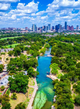 A view of Barton Springs Pool, a natural spring-fed pool in Zilker Park. People can be seen swimming and relaxing in the clear blue water, surrounded by lush greenery, making it a popular spot in the city.

