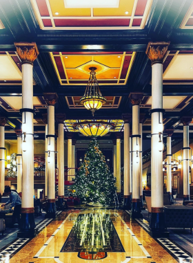 The interior of the historic Driskill Hotel, beautifully decorated for the holiday season with a towering Christmas tree surrounded by elegant decor. The lobby's ornate architecture enhances the festive atmosphere, inviting guests to experience the holiday spirit.

