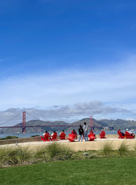 A panoramic view of the Presidio Tunnel Tops, showcasing beautifully landscaped parks with walking trails, picnic areas, and views of the Golden Gate Bridge. Families and friends are enjoying the open space on a sunny day.