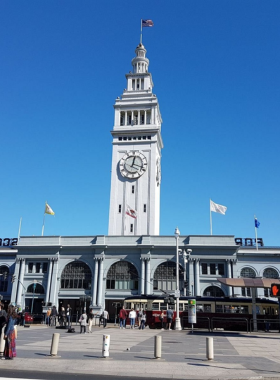  A vibrant scene of the Ferry Building Marketplace bustling with people shopping and dining. The iconic clock tower stands tall against the backdrop of a clear sky, while vendors display fresh produce and artisanal goods.