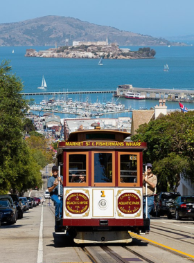 A classic San Francisco cable car traveling along a steep street, with Alcatraz Island visible in the distance. The vibrant red and gold of the cable car contrasts with the blue waters of the bay, encapsulating the charm of the city.