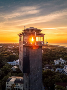  A stunning sunset over Sullivan’s Island, with the sun casting a warm glow over the tranquil waters. Silhouettes of palm trees frame the beach, creating a peaceful and picturesque scene of Charleston’s coastline.