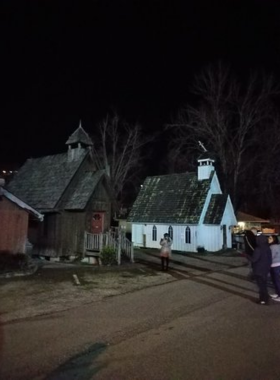 A spooky scene depicting a ghost and haunt tour in Gatlinburg, featuring a group of participants listening to a guide near a dimly lit historic building. The atmosphere is filled with intrigue and excitement as tales of local hauntings are shared.