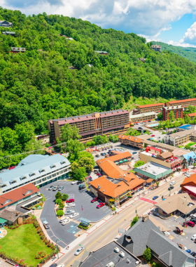 A vibrant view of downtown Gatlinburg showcasing bustling streets lined with charming shops and restaurants. The scene is set against a backdrop of lush green mountains, capturing the lively atmosphere of this popular tourist destination.